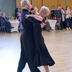 Tanzendes Paar in eleganter Kleidung auf einer Tanzfl&auml;che, umgeben von Zuschauern in einem festlichen Saal.