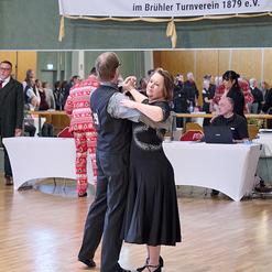 Tanzpaar in eleganter Kleidung tanzt auf einer Sportveranstaltung, im Hintergrund Zuschauer und ein Banner des TSC Br&uuml;hl.