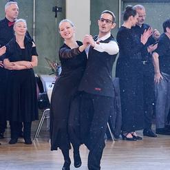 Tanzendes Paar in eleganter Kleidung auf einer Tanzfl&auml;che, umgeben von applaudierenden Zuschauern.