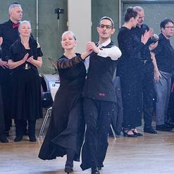Tanzpaar in eleganter Kleidung f&uuml;hrt einen Tanzschritt vor applaudierendem Publikum in einem festlichen Raum aus.