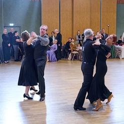 Tanzpaare in eleganter Kleidung tanzen auf einer Holzfl&auml;che w&auml;hrend einer Tanzveranstaltung, im Hintergrund Zuschauer.