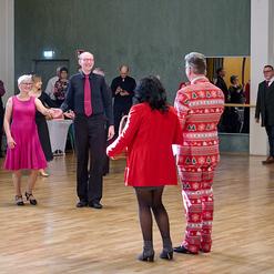 Tanzveranstaltung in einem Saal mit mehreren Teilnehmern, die in festlicher Kleidung miteinander tanzen.