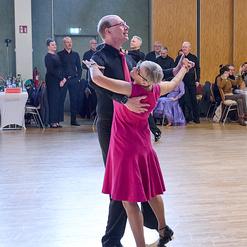 Tanzendes Paar in eleganter Kleidung auf einer Tanzfl&auml;che, umgeben von Zuschauerinnen und Zuschauern.