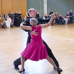 Tanzpaar in eleganter Tanzpose auf einer Holzfl&auml;che vor Publikum bei einer Tanzveranstaltung.