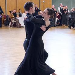 Tanzpaar in eleganter Kleidung f&uuml;hrt einen Paartanz in einem festlichen Saal mit applaudierendem Publikum aus.