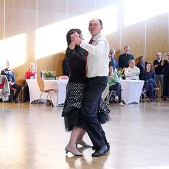 Tanzendes Paar in eleganter Kleidung auf einer hellen Tanzfl&auml;che, Zuschauer verfolgen aufmerksam.