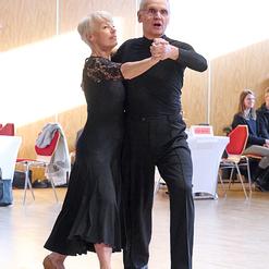 Tanzpaar in eleganter Kleidung f&uuml;hrt einen Paartanz auf einer Holzfu&szlig;bodenfl&auml;che in einem hellen Raum aus.