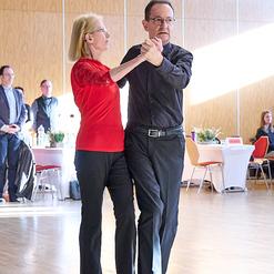 Tanzendes Paar in einem festlichen Saal, gehaltene H&auml;nde, Frauen in rotem Oberteil, Mann in schwarzem Hemd.