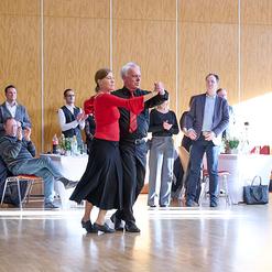 Tanzendes Paar in eleganter Kleidung, umgeben von applaudierenden G&auml;sten in einem festlichen Saal.