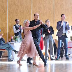 Tanzen eines Paares in eleganter Kleidung, umgeben von applaudierenden G&auml;sten in einem festlichen Raum.