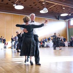 Tanzende Paare in eleganter Kleidung auf einer Tanzfl&auml;che in einem festlich dekorierten Raum. Publikum applaudiert.