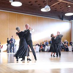Tanzende Paare in eleganter Kleidung auf einer Tanzfl&auml;che, umgeben von G&auml;sten an festlich gedeckten Tischen.