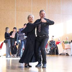 Tanzendes Paar in formeller Kleidung auf einer Tanzfl&auml;che, im Hintergrund weitere G&auml;ste und Tische.