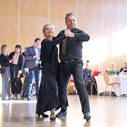 Tanzendes Paar in eleganter Kleidung auf einer Tanzfl&auml;che, im Hintergrund Zuschauer bei einer Veranstaltung.