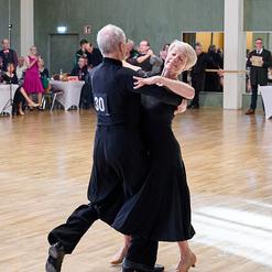 Tanzendes Paar in eleganter Kleidung auf einer Holzfl&auml;che, die sich anmutig umarmen und eine Tanzfigur ausf&uuml;hren.