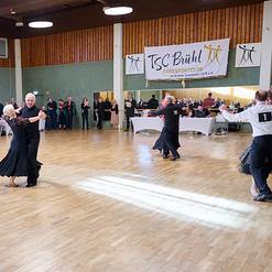 Tanzende Paare in eleganter Kleidung auf einer Holzfl&auml;che w&auml;hrend einer Veranstaltung im TSC Br&uuml;hl im Hintergrund.