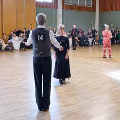 Tanzendende Paare in eleganter Kleidung auf einer Tanzfl&auml;che, im Hintergrund Zuschauer an Tischen.