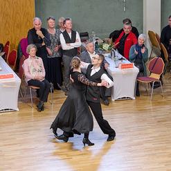 Tanzpaar in eleganter Kleidung tanzt auf einer Veranstaltung, w&auml;hrend das Publikum applaudiert und zuschaut.