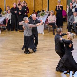 Tanzpaar in formeller Kleidung f&uuml;hrt einen Walzer auf einer Tanzfl&auml;che, umgeben von applaudierenden Zuschauern.