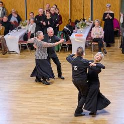 Tanzpaar in eleganter Kleidung f&uuml;hrt einen Walztanz auf einer Holz-Tanzfl&auml;che vor Publikum auf.