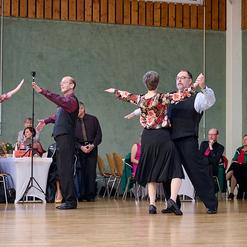 Tanzende Paare in eleganter Kleidung auf einer Tanzfl&auml;che, Zuschauer im Hintergrund applaudieren.