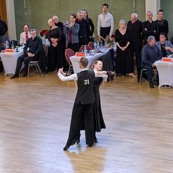 Tanzendes Paar in eleganter Kleidung bei einem Wettkampf, umgeben von zuschauenden G&auml;sten in festlicher Stimmung.