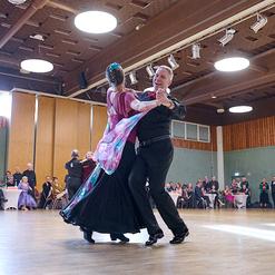 Tanzpaar in eleganter Kleidung tanzt auf Parkettboden vor zuschauendem Publikum in festlicher Atmosph&auml;re.