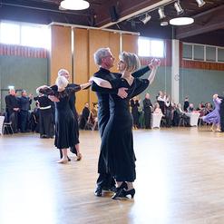 Tanzende Paare in eleganter Kleidung auf einer Tanzfl&auml;che, umgeben von Publikum in einem festlichen Saal.