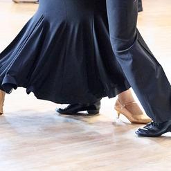 Tanzende Paare zeigen ihre F&uuml;&szlig;e, einer in schwarzen, der andere in beigen Schuhen auf glattem Parkettboden.