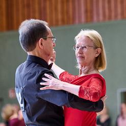 Tanzendes Paar in eleganter Kleidung w&auml;hrend einer Veranstaltung, der Mann tr&auml;gt ein schwarzes Hemd, die Frau ein rotes Kleid.