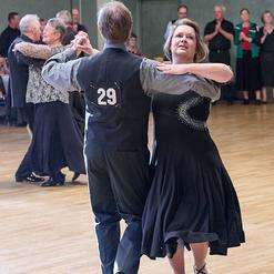 Tanzpaar in eleganter Kleidung bewegt sich zur Musik auf einer Tanzfl&auml;che, im Hintergrund applaudierende Zuschauer.