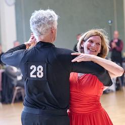 Tanzpaar inmitten eines Festsaals, der Mann tr&auml;gt eine schwarze Kleidung mit der Nummer 28, die Frau ein rotes Kleid.