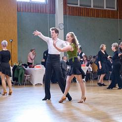 Tanzveranstaltung mit Paaren in eleganter Kleidung, die auf einer Tanzfl&auml;che zu Musik tanzen. Tische im Hintergrund.