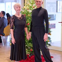 Tanzendes Paar in eleganter Kleidung steht vor einem geschm&uuml;ckten Weihnachtsbaum in festlicher Atmosph&auml;re.