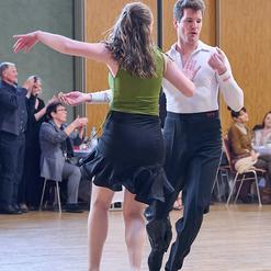 Tanzendes Paar in elegantem Outfit auf einer Tanzfl&auml;che, umgeben von Zuschauern bei einer Veranstaltung.