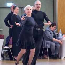 Tanzende Paare in eleganter Kleidung, Hintergrund mit Zuschauern und einer festlichen Atmosph&auml;re.