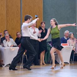 Tanzpaar in eleganter Kleidung beim Tanzwettbewerb, Zuschauer im Hintergrund applaudieren.