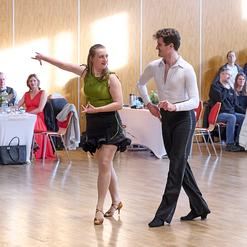 Tanzpaar in auff&auml;lliger Kleidung pr&auml;sentiert einen Paso Doble in einem hellen Saal vor einer Zuschauergruppe.