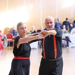 Tanzendes Paar in eleganter Kleidung, umgeben von Zuschauern in einem Veranstaltungsraum.
