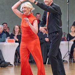 Tanzendes Paar in eleganter Kleidung auf einer Tanzfl&auml;che, umgeben von Zuschauern bei einem Wettbewerb.