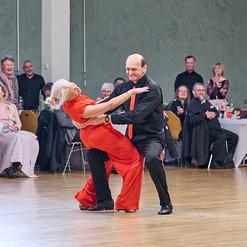 Tanzpaar f&uuml;hrt einen leidenschaftlichen Tanz auf einer Veranstaltung, umgeben von applaudierendem Publikum.