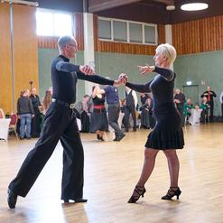 Tanzpaar bewegt sich elegant auf einer Tanzfl&auml;che, umgeben von Zuschauern in einem festlichen Saal.