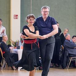 Tanzender Mann und Frau in eleganter Kleidung auf einer Tanzfl&auml;che, umgeben von applaudierendem Publikum.