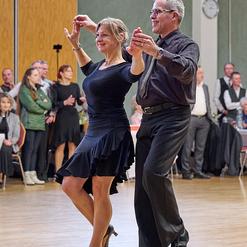 Tanzpaar f&uuml;hrt einen Paso Doble auf einer Tanzfl&auml;che, umgeben von Zuschauern in festlicher Kleidung.