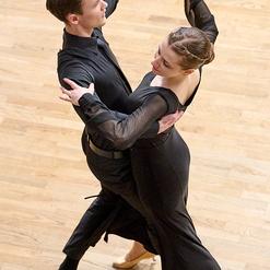 Paar in eleganter Tanzkleidung tanzt eng umschlungen auf einem Holzfu&szlig;boden.