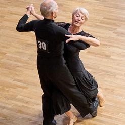 Tanzendes Paar in eleganter Kleidung auf einem Holzboden, Frau mit leicht frisiertem Haar l&auml;chelt.