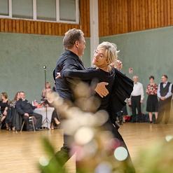 Tanzendes Paar in eleganter Kleidung auf einer Tanzfl&auml;che, umgeben von G&auml;sten in festlicher Atmosph&auml;re.