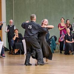 Tanzpaar in eleganter Kleidung tanzt auf einer Veranstaltung, umgeben von applaudierendem Publikum.