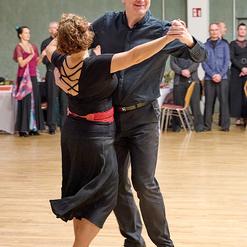 Tanzpaar in eleganter Kleidung, das auf einer Holzfl&auml;che t&auml;nzerisch miteinander interagiert. Hintergrund mit Zuschauern.