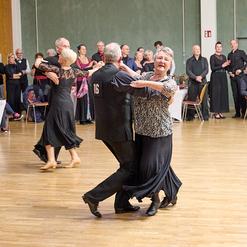Tanzende Paare auf einer Tanzfl&auml;che, umgeben von Zuschauern in festlicher Kleidung. Atmosph&auml;rische Veranstaltung.
